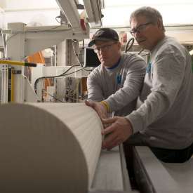 两名工人在机械上操纵实心的、原木大小的陶瓷材料